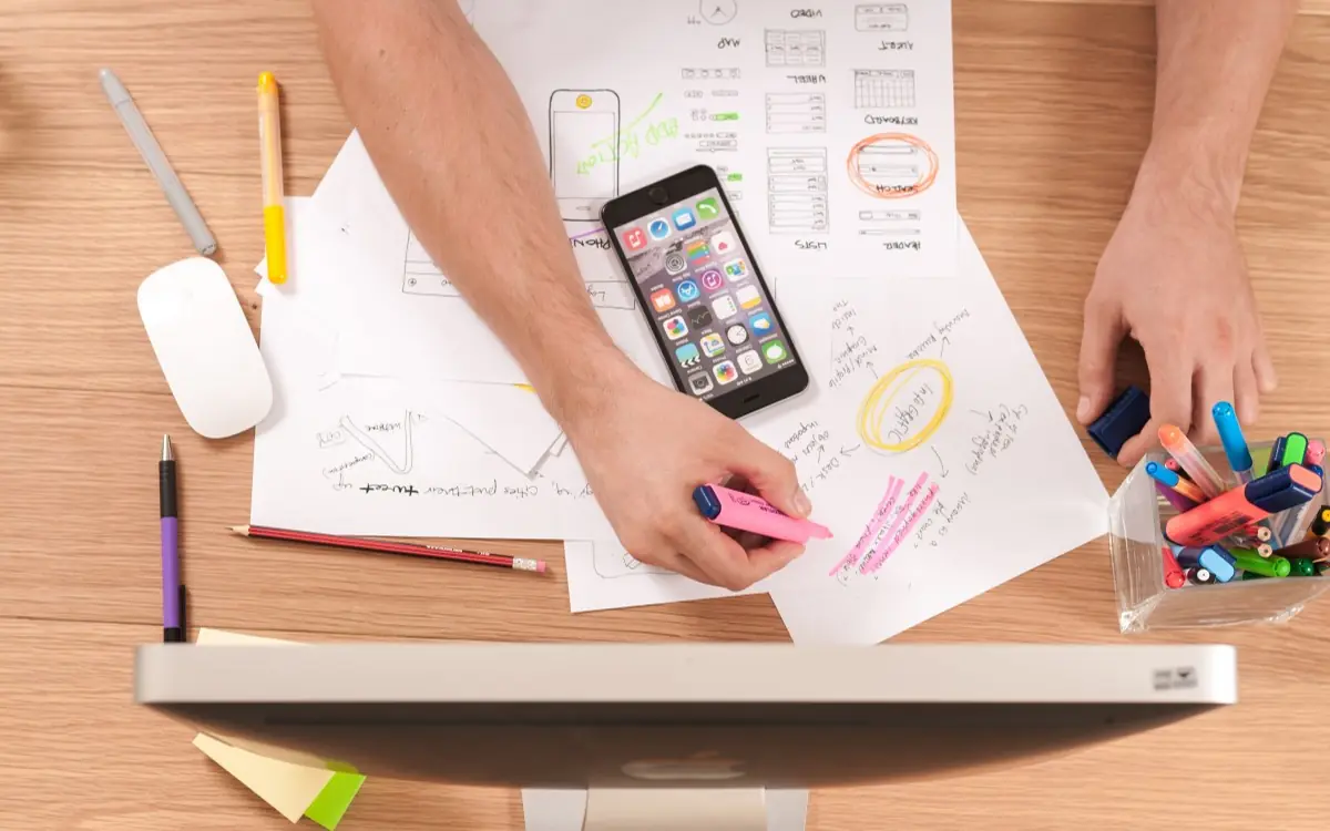 Hands sketching interface layouts on paper next to a smartphone